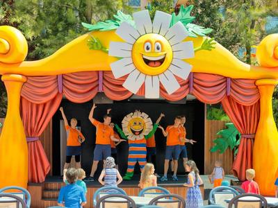 Plenerowy spektakl kukiełkowy na kolorowej scenie z dziećmi oglądającymi w parku.