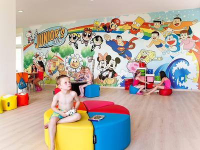 Dzieci bawiące się w kolorowej sali zabaw z muralami kreskówkowymi na ścianach.