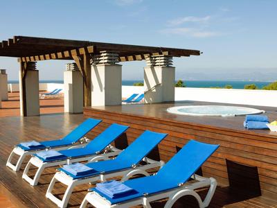 Niebieskie leżaki ustawione obok jacuzzi na drewnianym tarasie pod pergolą.