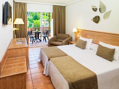 Przytulny pokój hotelowy z dwoma łóżkami, fotel, drewniane meble i balkon z stołem i krzesłami.