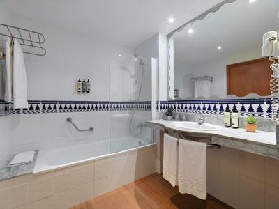 Czysta łazienka hotelowa z wanną, dużym lustrem, wieszakiem na ręczniki i nowoczesnym oświetleniem.