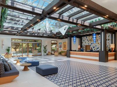 Nowoczesna lobby hotelowa z szklanym sufitem, częścią wypoczynkową i recepcją.