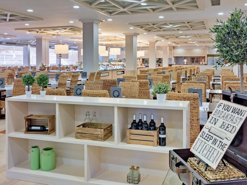 Nowoczesny hotelowy salon z wiklinowymi krzesłami, roślinami i dekoracyjnymi tabliczkami na półkach.