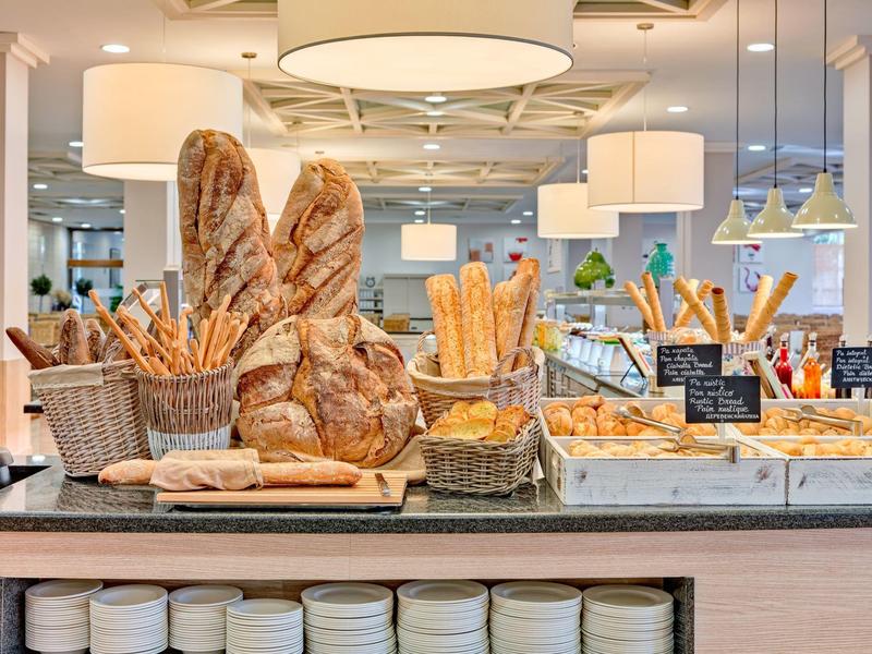 Różnorodne świeże pieczywo i bagietki ułożone w koszykach na hotelowym bufecie.