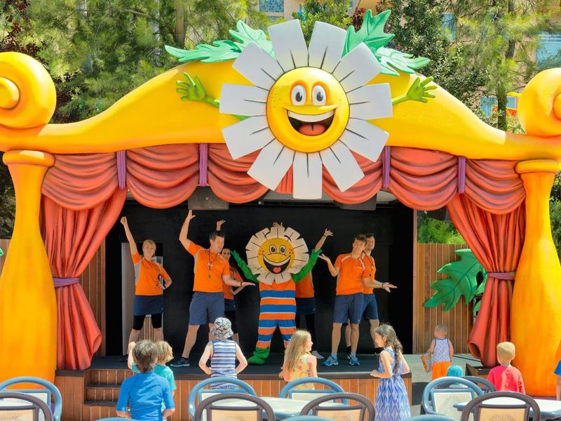 Plenerowy spektakl kukiełkowy na kolorowej scenie z dziećmi oglądającymi w parku.