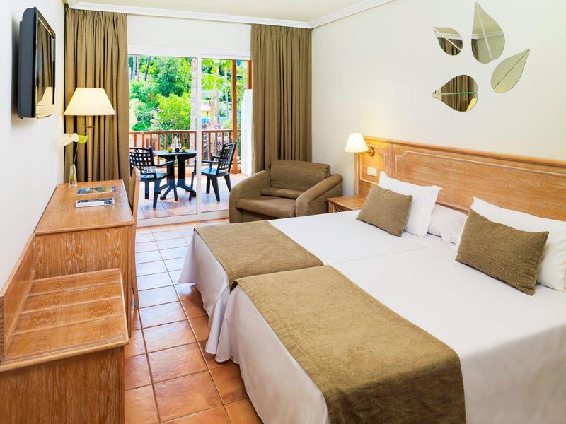 Przytulny pokój hotelowy z dwoma łóżkami, fotel, drewniane meble i balkon z stołem i krzesłami.