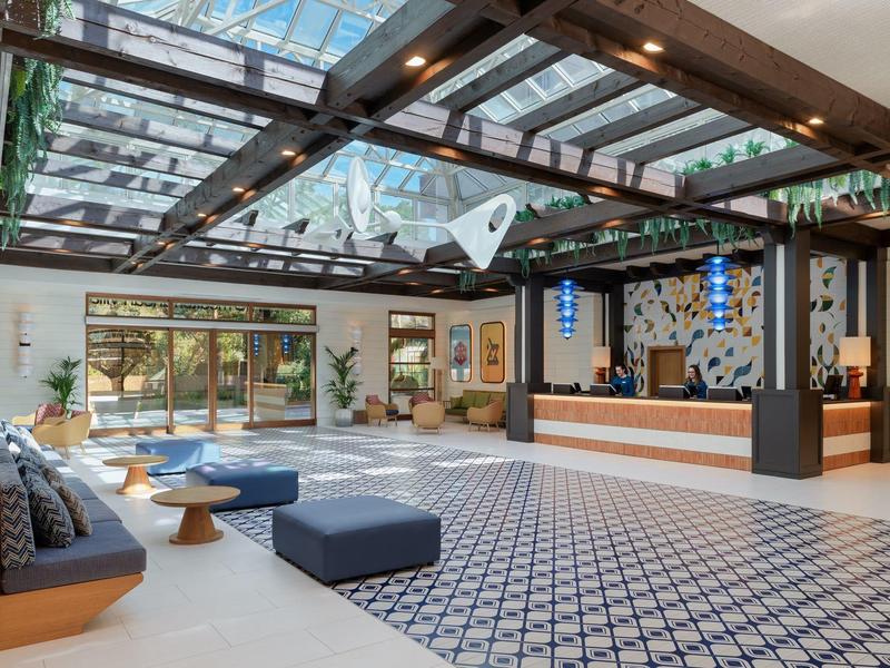 Nowoczesna lobby hotelowa z szklanym sufitem, częścią wypoczynkową i recepcją.