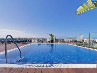 Piscine à débordement avec vue urbaine et ciel bleu clair.