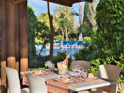 Terrasse d'hôtel avec une table dressée, vue sur la piscine et végétation luxuriante.