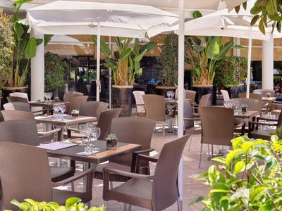 Terrasse de restaurant en plein air avec tables, chaises et parasols blancs.