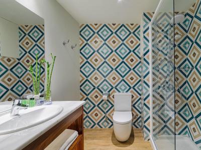 Salle de bain moderne avec carrelage géométrique, lavabo, miroir et cabine de douche vitrée.