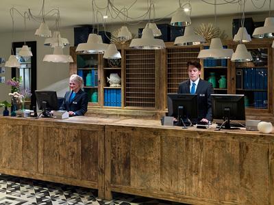 Réception d'hôtel classique avec deux réceptionnistes et un comptoir en bois robuste.