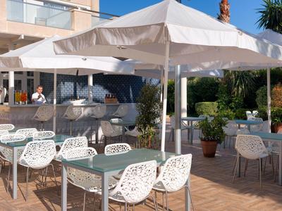 Terrasse de restaurant d'hôtel avec parasols blancs et chaises design en osier.