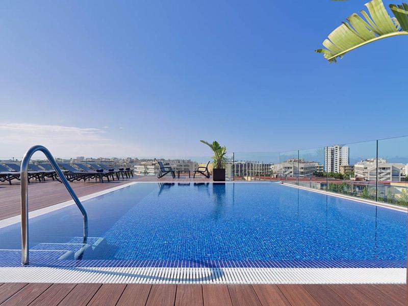 Piscine à débordement avec vue urbaine et ciel bleu clair.
