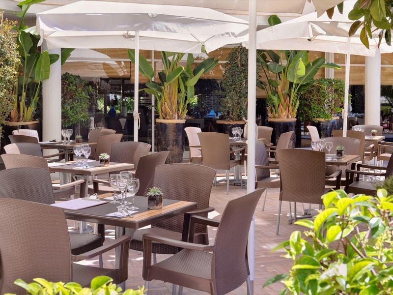 Terrasse de restaurant en plein air avec tables, chaises et parasols blancs.
