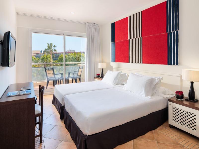 Chambre d'hôtel lumineuse avec deux lits, balcon et décoration moderne rouge et bleue.