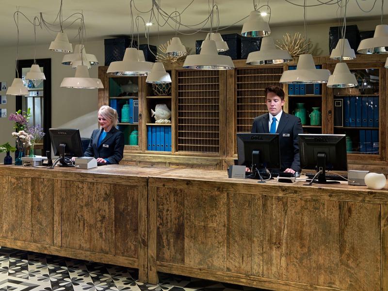Réception d'hôtel classique avec deux réceptionnistes et un comptoir en bois robuste.