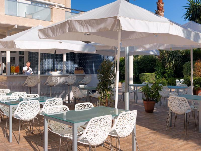 Terrasse de restaurant d'hôtel avec parasols blancs et chaises design en osier.