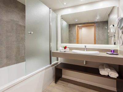 Moderní koupelna s vanou, velkou zrcadlovou stěnou a umyvadlem v neutrálních barvách.