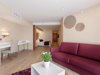 Moderní hotelový prostor s fialovou pohovkou, stolem s rostlinou a psacím stolem se židlemi.