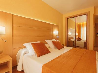 Pohodlný hotelový pokoj s manželskou postelí, oranžovými polštáři a přikrývkou, nočními stolky a zrcadlem.