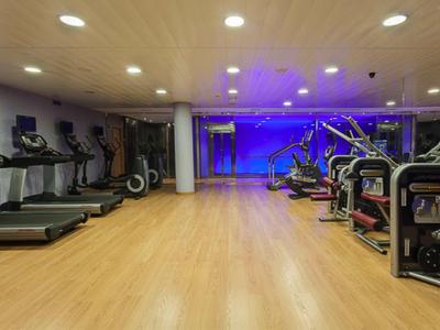 Salle de sport moderne avec tapis de course et équipements de fitness sur sol en bois et éclairage bleu.