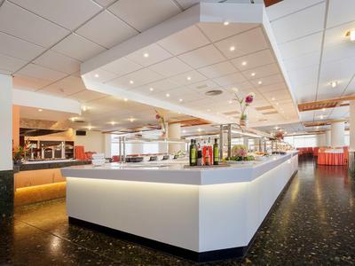 Moderní hotelový bar se osvětleným pultem a červeným posezením v jasné místnosti.