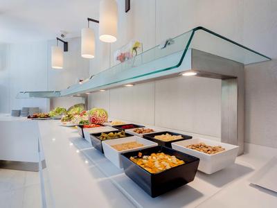 Bufet s různými pokrmy v moderních černých a bílých miskách pod skleněným krytem.