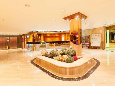 Světlá hotelová hala s recepcí a centrální květinovou výzdobou na světlé podlaze.