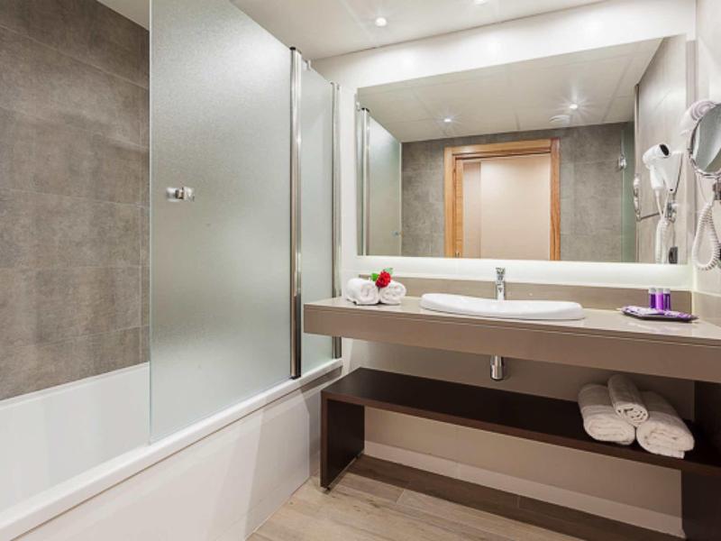 Moderní koupelna s vanou, velkou zrcadlovou stěnou a umyvadlem v neutrálních barvách.