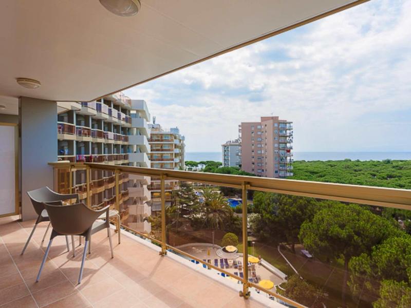 Balkon s stolem a židlemi s výhledem na bytové domy a zeleň u moře