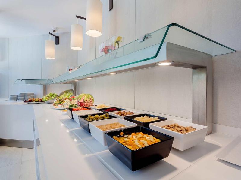 Bufet s různými pokrmy v moderních černých a bílých miskách pod skleněným krytem.