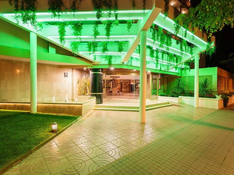 Vstup do hotelu osvětlený zeleně s moderní střechou a okolím v noci.