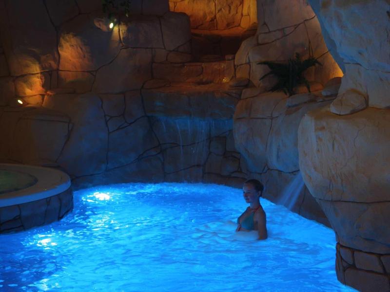 Osvětlený bazén v skalní jeskyni s uvolněným plavcem.