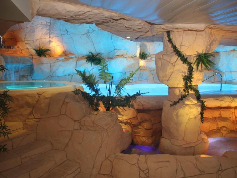 Vnitřní bazén s kamennými stěnami a exotickou výzdobou v relaxační hotelové atmosféře.