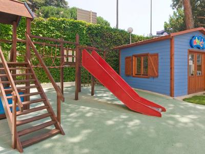 Área de juegos con tobogán, estructura para escalar y pequeña casita azul y roja en zona verde