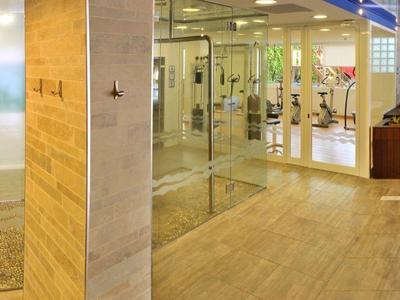 Área de spa moderna con paredes de vidrio, sauna y suelo de madera clara en un hotel.