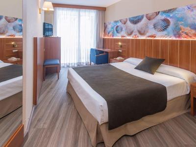 Habitación doble con cama, manta oscura, mesitas y ventana con cortinas translúcidas