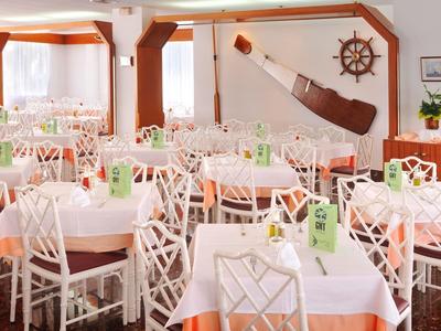 Comedor bien iluminado con varias mesas puestas y sillas blancas en un hotel.