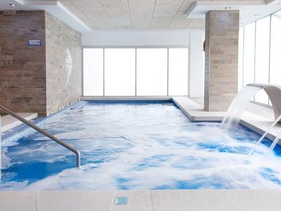 Piscina interior moderna con cascada y bancos de burbujas en un hotel.