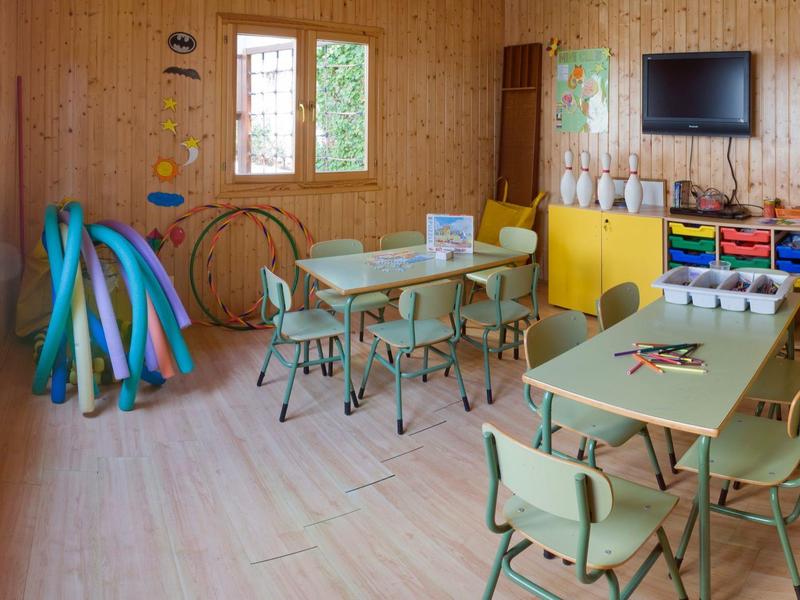 Sala infantil con mesas pequeñas, sillas y juguetes coloridos en las paredes.