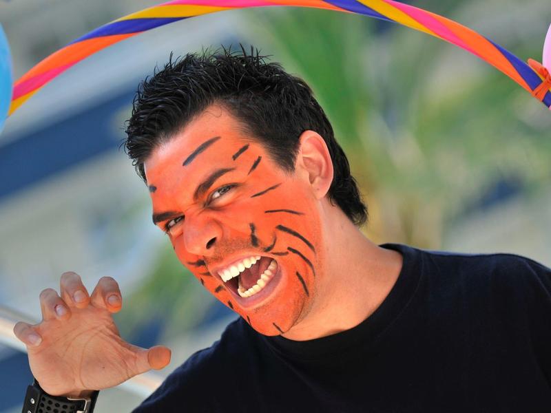 Hombre con pintura facial naranja y rayas negras, sonriendo y posando, ambiente vacacional.