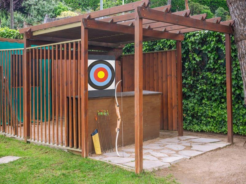 Área de tiro con arco con diana en un jardín al lado de un cobertizo de madera y árboles.