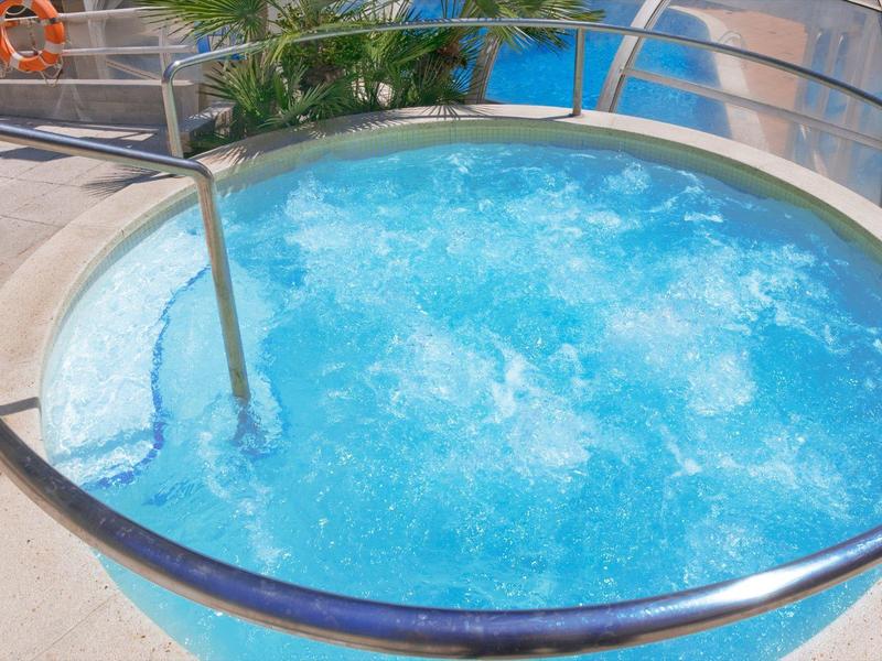 Jacuzzi redondo con agua burbujeante y barandilla metálica junto a una piscina del hotel.
