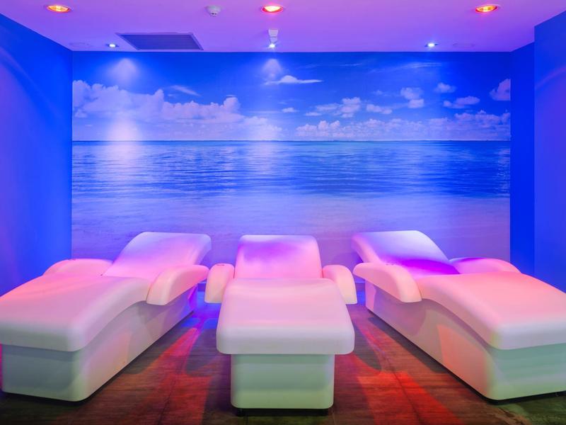 Tres tumbonas blancas en una habitación con luz azul y un mural de mar y cielo.