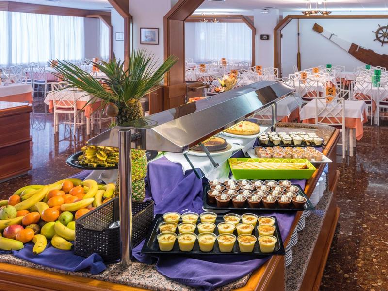 Zona de buffet en un restaurante con frutas, ensaladas y postres, con una decoración luminosa y acogedora.
