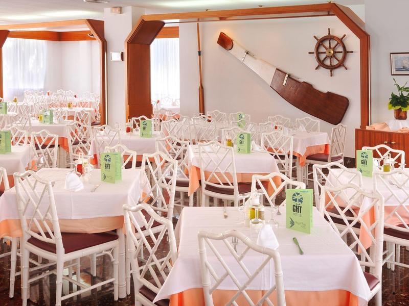 Comedor bien iluminado con varias mesas puestas y sillas blancas en un hotel.