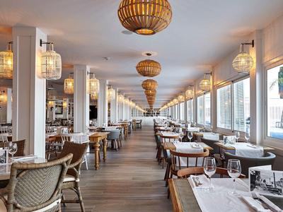 Comedor luminoso en un hotel moderno con muchas mesas y lámparas de mimbre.