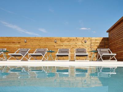 Área de piscina moderna con seis tumbonas grises y revestimiento de madera bajo un cielo despejado.