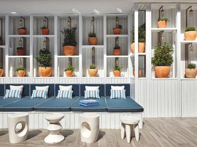 Moderner Sitzbereich mit blauen Polstern, weißen Tischen und Regalen mit Pflanzen in Terrakottatöpfen.